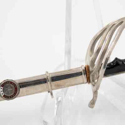 An up close image of the miniature Texas A&M saber hilt.: Image of the miniature saber sitting on a clear stand. The image is a detail view of the hilt and small leather piece on the end of the scabbard.