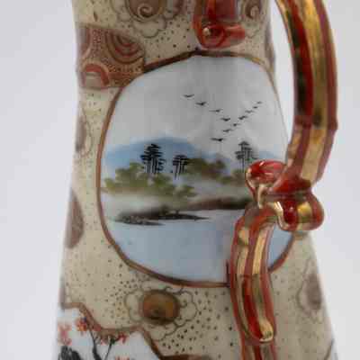 Painted Japanese porcelain teapot and lid scene.: Up close image of the gold and red painted teapot with matching lid. It is decorated with an image of of coastal scene and shows trees by the water.