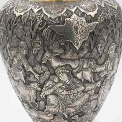 Scene on the silver and brass urn from Persia.: Up close image of the debossed scene on the silver urn. The scene depicts a woman comforting a child and a donkey in the background. There is also a man herding an ox.