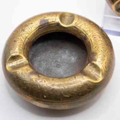 Ashtray: The image shows round brass ashtrays with intricate leaf designs engraved along the rims.