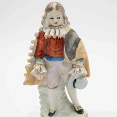 Painted Japanese porcelain figurine of a boy.: Up close image of the painted Japanese porcelain figurine of a boy dressed in colonial-style garments and holding a hat.