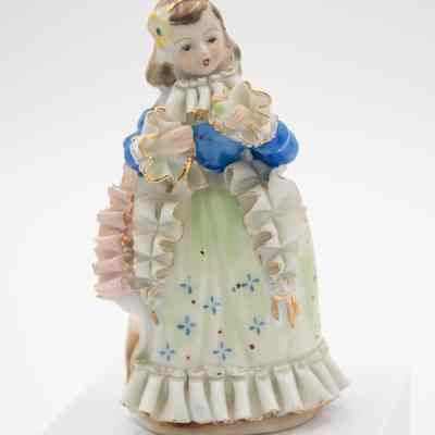 Painted Japanese porcelain figurine of a girl.: Up close image of the painted Japanese porcelain figurine of a girl dressed in colonial-style garments and holding a flower.