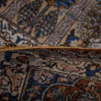 Large cream and blue area rug with deer: The image shows a folded portion of a detailed, cream and blue area rug adorned with intricate patterns.