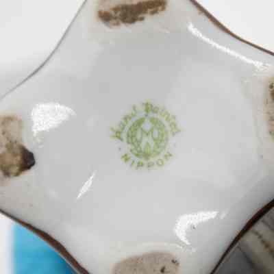 Bottom of the small Nippon Japanese porcelain vase given to the Jordans by the Prime Minister of France.: Up close image of the bottom of the porcelain vase. There is remnants of dirt where it was resting on a  surface. There is a green stamp in the center that reads "Hand Painted NIPPON."