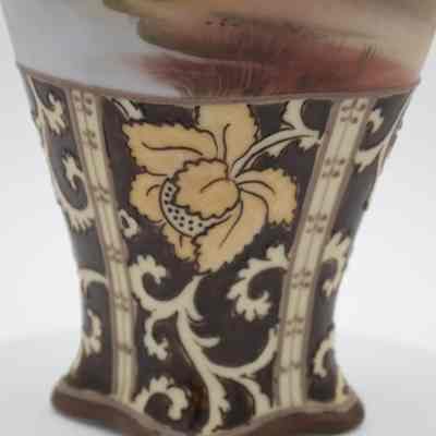 Pedestal base of the small Nippon Japanese porcelain vase given to the Jordans by the Prime Minister of France.: Up close image of the brown and gold vase. The base is brown and there are yellow gold swirls and a flower on top. There are raised line details across the yellow gold details.