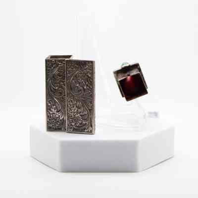 Silver Italian lipstick box gifted to Mrs. Jessie Jordan by the queen consort of Iran.: Image of the front and inside of the silver Italian lipstick box. The box is intricately decorated with floral vine designs and the lipstick on the inside is a fire engine red.