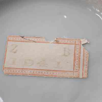 Bottom of the painted Japanese porcelain teapot.: Up close image of a sticker on the bottom of the porcelain teapot. It cream-colored with red trip and stamped with the letters "ZB" and the number "1941."