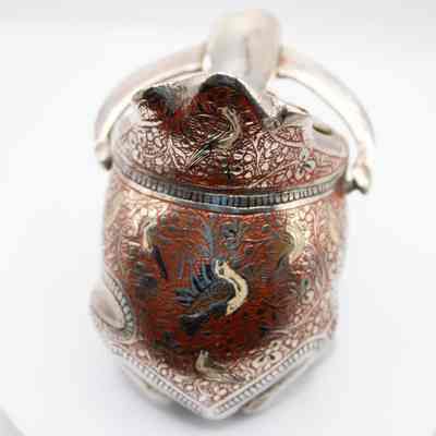 Top of frog ashtray: The silver frog ashtray displays intricate red designs with birds and floral patterns adorning its surface.