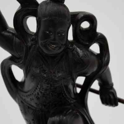 The man in the carved ebony figurine.: Up close image of the dark brown wood man standing on the sea monster. The man's clothing is intricately carved and his hair is in a bun. Both the sea monster and his eyes and teeth are white ivory.