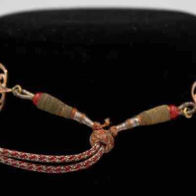 Clasp on the necklace given to Mrs. Jessie Jordan by Her Highness Badriah Al-Ahmad Al-Jaber Al-Mubarak Al-Sabah.: Up close image of the clasp on the necklace. There are two cords attached by a small ring. The cords are red, silver, and brown, and the ring is orange and silver.