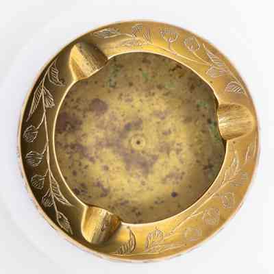 Top view of ashtray: The image depicts a small brass ashtray with an engraved floral and leaf design around the rim.