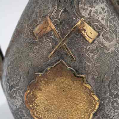 Bronze decorations on the silver coffee pot given to the Jordans by a Kuwaiti ruler.: Up close image of the bronze decorations on the silver coffee pot. There are two cross flags with Arabic script that reads "Kuwait."