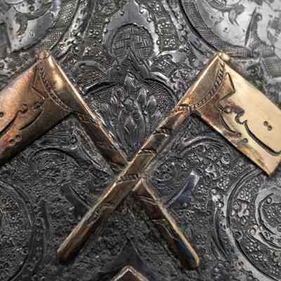 Bronze flag decorations on the silver coffee pot given to the Jordans by a Kuwaiti ruler.: Up close image of the crossed bronze flags with Arabic script on the silver coffee pot. The script on the flags translates to "Kuwait."
