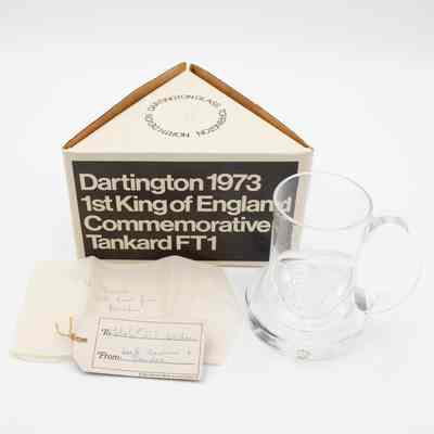 Side of triangle box, Dartington Glass tankard, and notes.: Image of the glass tankard pressed with King Edgar's head. There is a small sticker on the bottom that says "Dartington England." Two notes found with the tankard. The card reads "To: Mr. + Mrs. L.T. Jordan" and "From: Jack, Nadine, + Deirdre." The tissue paper reads "To Jessie with love from Deirdre." The side of the box reads "Dartington 1973 1st King of England Commemorative Tankard FT1."