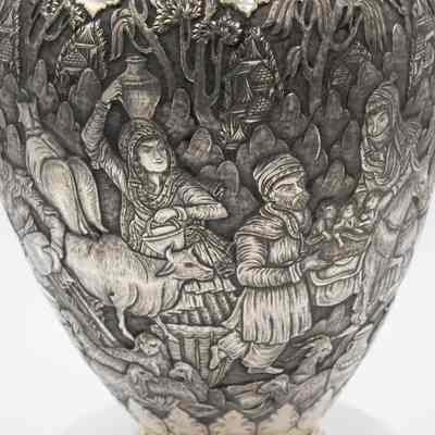 Scene on the silver and brass urn from Persia.: Up close image of the debossed scene on the silver urn. The scene depicts two women walking, one is holding an urn on her head. There is a man carrying a basket with three children in it. There are also multiple sheep around the bottom.