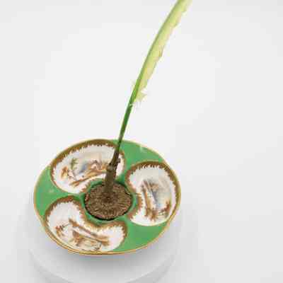 White and green quill stand: A white and green ceramic plate features a brass quill stand with a green quill. Each section of the plate has a landscape scene painted into it, with gold detailing around each.