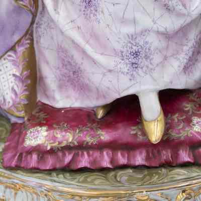 Base of figure: A porcelain figurine with purple gown sits gracefully on a rose pillow, adorned with gold embellishments and shoes.