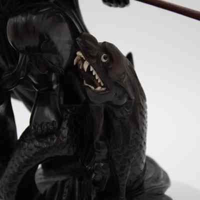 The sea monster in the carved ebony figurine.: Up close image of the dark brown wood figurine of the sea monster. It is roaring up and the eyes and teeth of the creature are white ivory.