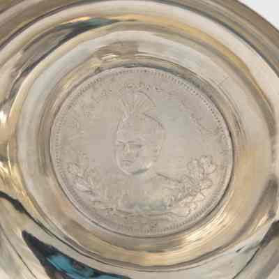 Small silver coin bowl with a coin of Shah Ahmad Qajar. Qajar was the Shah of Persia from 1909-1925 and was the last ruling member of the Qajar dynasty.: Up close image of the coin inside the silver coin bowl depicting Shah Ahmad Qajar of Persia.