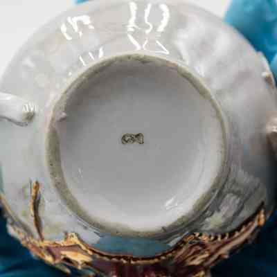 Bottom of tea cup: The image shows gloved hands holding the underside of a decorative cup.