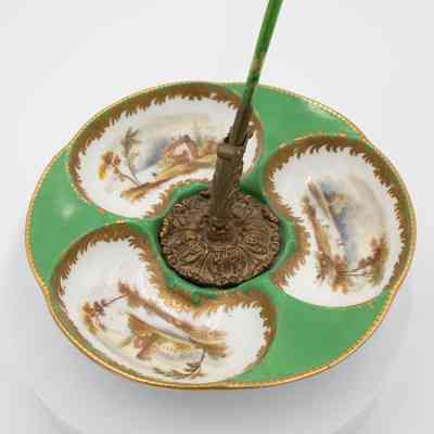 White and green quill stand: A white and green ceramic plate features a brass quill stand with a green quill. Each section of the plate has a landscape scene painted into it, with gold detailing around each.