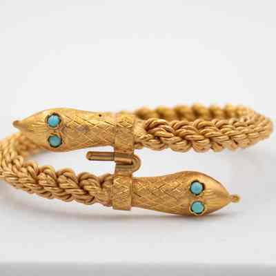Gold and turquoise snake bracelet.: Up close image of the gold corded bracelet with a snake head at either end. The snakes have blue turquoise eyes.