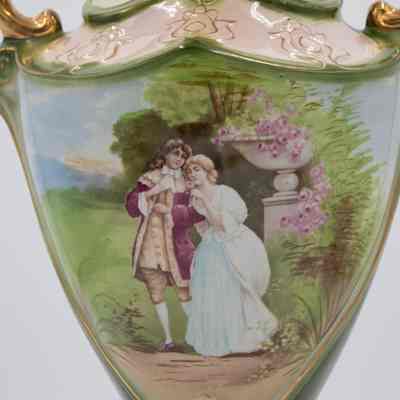 Painted scene on porcelain amphora-style vase that belonged to Mrs. Jessie Jordan's mother,: Up close image of the painted scene on the amphora-style vase. The scene is of a man and woman in colonial-style dress in a garden. The woman in holding a pink flower.