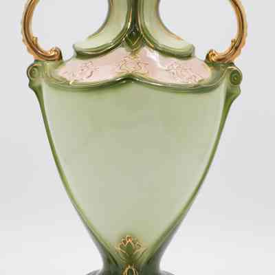 Back side of the green porcelain amphora-style vase that belonged to Mrs. Jessie Jordan's mother.: Image of the back of the light and dark green amphora-style vase. The vase has gold details in a lotus flower at the base and gold handles. The middle part is light green and not painted as the front is.