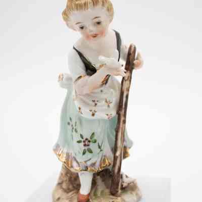 Girl painted porcelain figurine.: Image of one of two hand-painted porcelain figurines depicting a girl dressed in romantic-era fashion. She is holding a stick and playing with a small white bird, likely a dove.