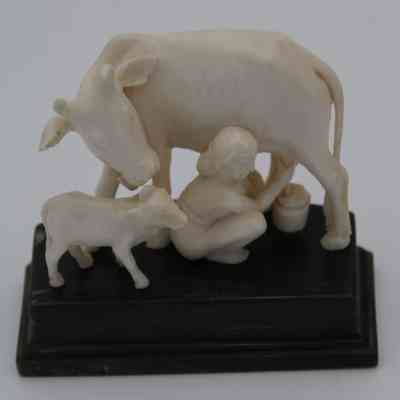 Close up of ivory figure of a child milking a cow: An ivory figure depicts a child milking a cow, accompanied by a calf.