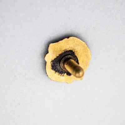 The back of the Lions Club pin.: Image of the gold back of the Lions Club pin with black tarnish around the post. There is small, illegible text embossed on the back.