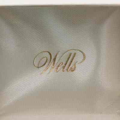 The inside of the Lions Club pin box.: Image of the inside top cover of the Lions Club pin box. The text reads "Wells" in gold cursive on a white satin background.