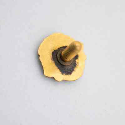 The back of the Lions Club pin.: Image of the gold back of the Lions Club pin with black tarnish around the post. There is small, illegible text embossed on the back.