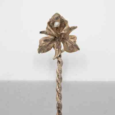 Orchid topper of 1932 Bolivar spoon.: The image is a close up of the spoons topper, which is an orchid flower. It features three prominent petals, three smaller petals and a pearl attached to the most prominent top petal.