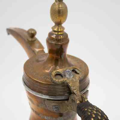 Coffee pot lid: The image shows a brass coffee pot with a leather-woven handle and intricate Arabic script.