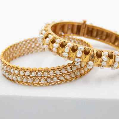 Jessie Jordan's gold and pearl bracelets: Up close image of two gold and pearl bracelets sitting on a white block. One with two "channels" of pearls around bracelet and one with multiple rows of pearls set across the band.