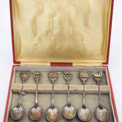 Set of six coffee spoons paired in sets of two with three designs.: Image of the set of six silver coffee spoons with two depicting Arabian camels, two with Arabic script, and two with abstract Kuwaiti dhows. They are resting on beige felt in a red case and yellow satin lid.
