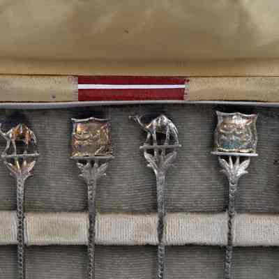 Handles of the six coffee spoons.: Up close image of the handles of the six silver coffee spoons with two depicting Arabian camels, two with Arabic script, and two with abstract Kuwaiti dhows.