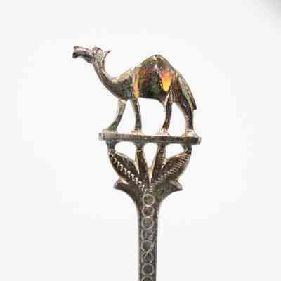 Camel on one of the spoon handles.: Up close image of one of the spoon handles depicting a camel. Under the camel, the handle is decorated with debossed dots and engraved leaves.