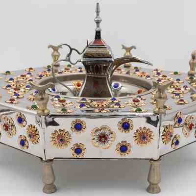 Stainless steel brazier gifted to Mrs. Jessie Jordan by Sheikh Sabah III Al-Salim Al-Sabah.: Image of stainless steel decorated with gold flowers and gem stones. The teapot is painted with gold and red designs and the brazier sits on bronze pedestal legs.