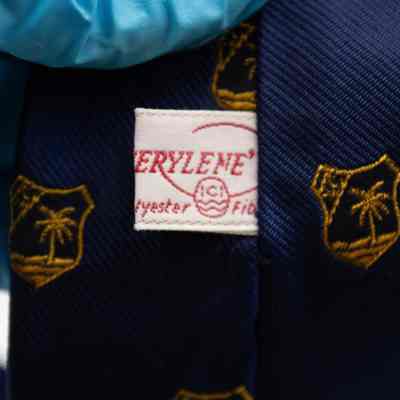 Tag of the Nakhlistan Club necktie.: Up close image of the white tag on the back of the navy blue tie. It is printed with red letters and reads "100% TERYLENE Throughout Polyester Fibers."