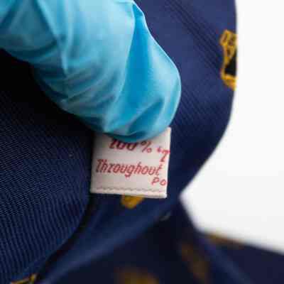 Tag of the Nakhlistan Club necktie.: Up close image of the white tag on the back of the navy blue tie. It is printed with red letters and reads "100% TERYLENE Throughout Polyester Fibers."