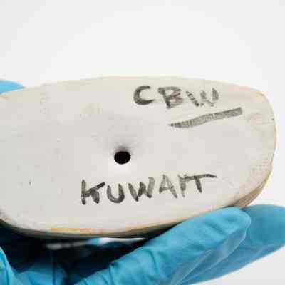 Bottom of ceramic: The image depicts the base of a ceramic figurine, featuring the words "CBW" and "KUWAIT" written in black ink.