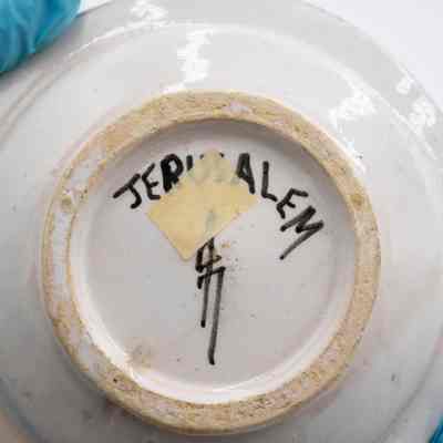 Bottom of one of the ceramic ashtrays given to the Jordans by a ruler in Bombay.: Up close image of the bottom of one of the ceramic ashtrays. It is painted with "JERUSALEM" and the artist signature. Additionally there is a piece of yellow masking tape.