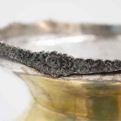 Edge of the large silver and brass urn from Persia.: Up close image of the debossed edge of the silver urn. It is intricately decorated with a floral pattern.
