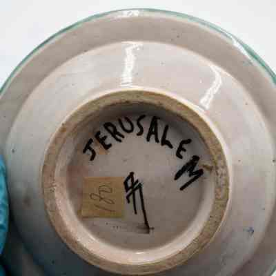 Bottom of one of the ceramic ashtrays given to the Jordans by a ruler in Bombay.: Up close image of the bottom of one of the ceramic ashtrays. It is painted with "JERUSALEM" and the artist signature. Additionally there is a piece of yellow masking tape with the number "180" written on it.