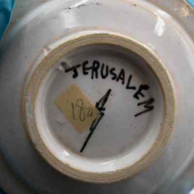 Bottom of one of the ceramic ashtrays given to the Jordans by a ruler in Bombay.: Up close image of the bottom of one of the ceramic ashtrays. It is painted with "JERUSALEM" and the artist signature. Additionally there is a piece of yellow masking tape with the number "180" written on it.
