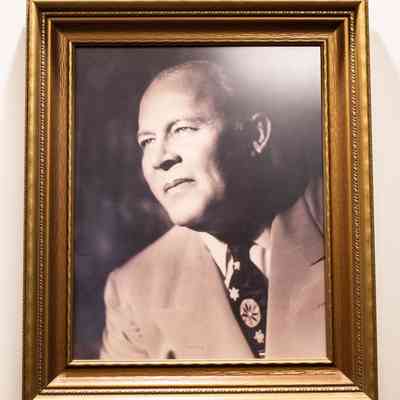 Framed photo of Leland T. Jordan: A framed photo of L.T. Jordan in a gold frame. He wears a pale suit with an accented tie.