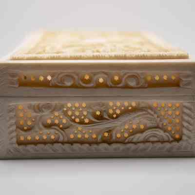 Side of the carved ivory dragon box from India.: Up close image of one of the sides of the rectangular ivory box. There are small cutouts and a dragon tail carved.