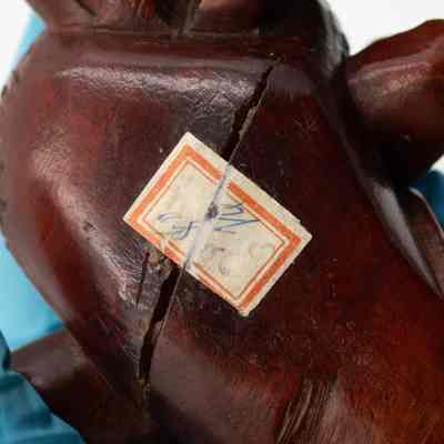 Bottom of one of the carved red wood goldfish.: Up close image of the bottom of one of carved goldfish. There is a discolored sticker with red trim and handwritten text that is illegible.